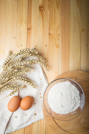 eggs and ears of wheat lie on a white canvas. Next to a bowl of flour on a round wooden stand. Agricultural still life on a light backgroundの写真素材