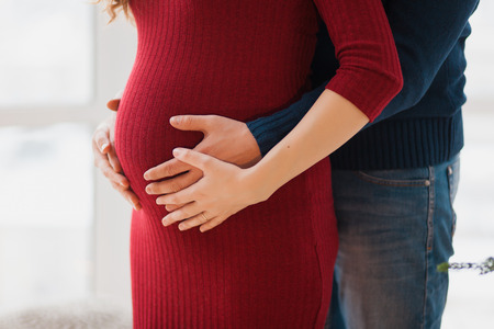Close up of parents hands touching pregnant belly at home, Woman in red dressの写真素材