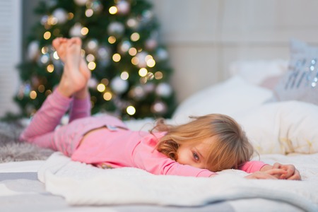 Cute little girl in pink pajamas on the bed in the morningの写真素材