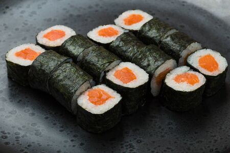 Hosomaki rolls closeup on a black plate with selective focus. Rolls with seaweed, rice, salmonの写真素材