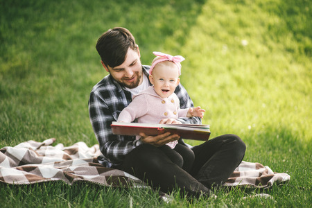 Father and his little baby daugter playing on a green grass in a park.の写真素材