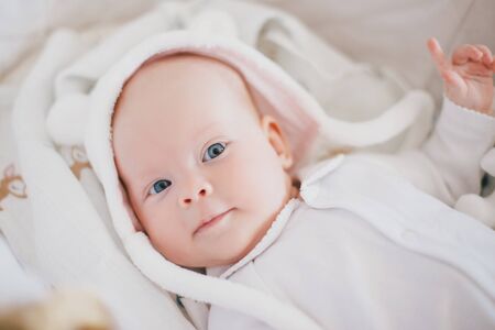 Little cute baby girl wearing white suit smiling in a straw basketの写真素材