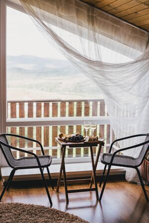 Table with wine, cheese, bread, grapes and pears standing on a cozy balcony in a wooden country...