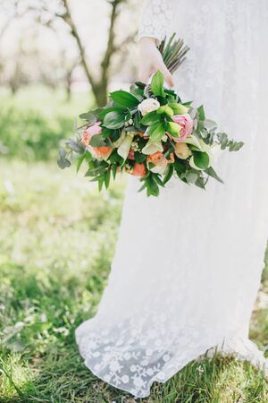 Bride holding wedding bouquet standing on the green grass in a garden.の写真素材
