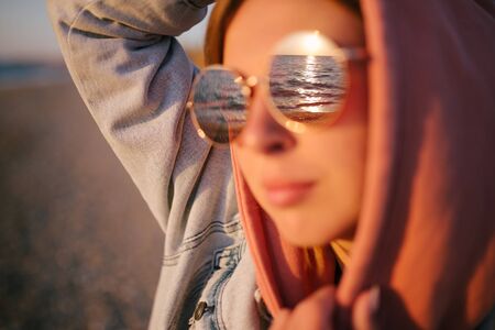 Young beautiful happy woman wearing sunglasses having good time at the beach on sunset timeの写真素材