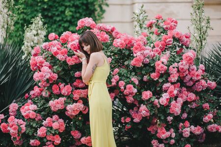 Young beautiful stylish woman in yellow jumpsuit with tattoo on her hand posing near roses flowers in a garden.の写真素材