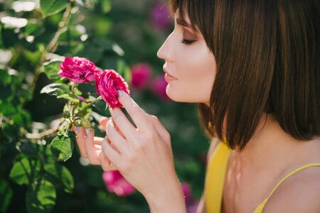 Young beautiful woman portrait close up with perfect skin posing with pink roses flowers in a garden.の写真素材
