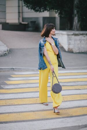 Young beautiful fashion woman wearing stylish yellow jumpsuit posing on european city streets.の写真素材