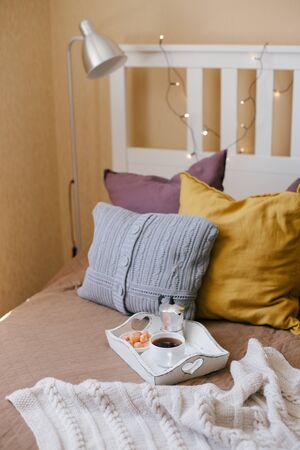 Still life with hot coffee and kumquat on wooden tray standing on bed with cozy lights on the background.の写真素材