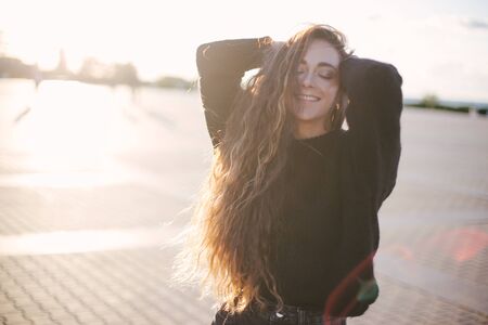 Young beautiful happy woman with long curly hair smiling and enjoying sunlight and warm sunny weatherの写真素材
