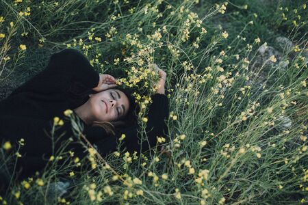Young beautiful woman with a bright shining glittering make up lying on a green meadow with yellow flowers.の写真素材