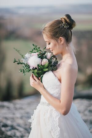 Young beautiful bride posing with wedding bouquet with gorgeous nature view on the background.の写真素材