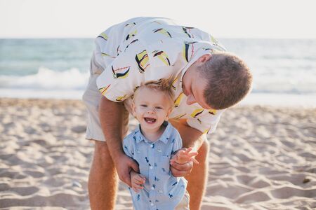 Young father having fun with his little son on beach at sunset.