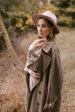 Beautiful young woman wearing fashion clothes and stylish hat posing near lake in beautiful autumn forest.の写真素材