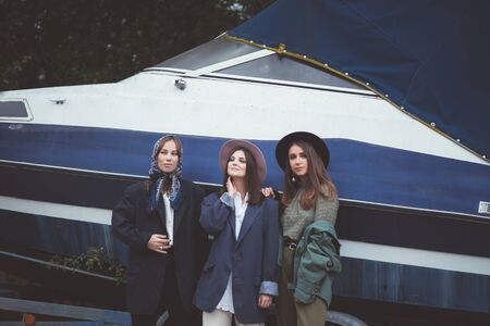 Three stylish young women wearing fashion clothes and stylish hats posing in beautiful yard. Female friendship concept.の写真素材
