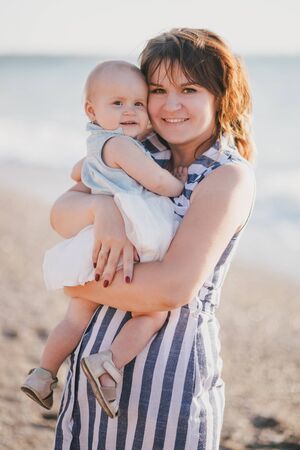 Happy young mother posing with her baby daughter near sea at beach.の写真素材