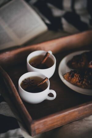 Two cups of tea with cinnamon sticks and anise stars and two croissants on a plate in a cozy roomの写真素材