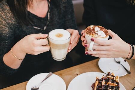 Two young women drinking coffee together in a cozy cafe.の写真素材