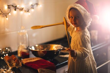 Cute baby girl in Santa Claus hat making Christmad cookies on decorated kitchenの写真素材