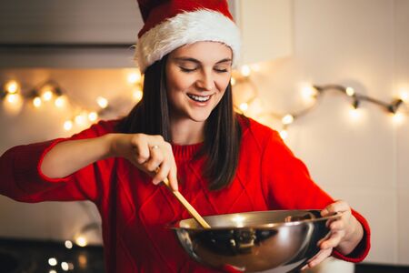 Young beautiful happy woman in Santa hat cooking Christmas cookies on holiday decorated kitchen.の写真素材