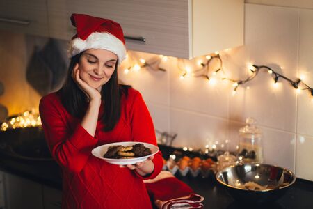 Young beautiful happy woman in Santa hat cooking Christmas cookies on holiday decorated kitchen.の写真素材