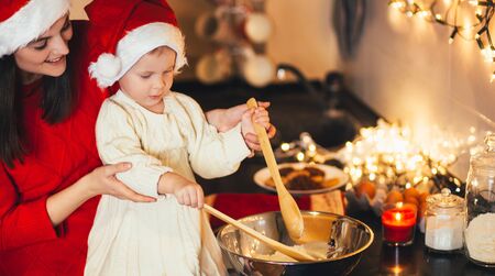 Happy mother and her baby daughter making Christmas cookies on holiday decorated kitchen.の写真素材