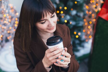 Young beautiful stylish woman drinking coffee on Christmas decorated city street.の写真素材