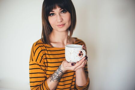 Beautiful young woman with tattoo drinking coffee or tea on white background.