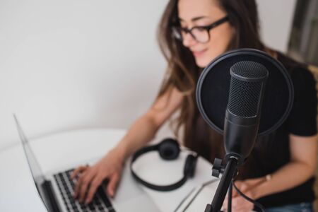 Attractive young woman blogger with long black hair recording online podcast using her laptop,...