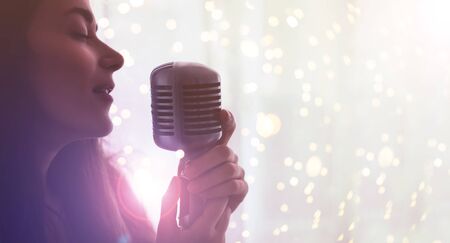 Young beautiful woman sing in vintage microphone with lights on background.の写真素材
