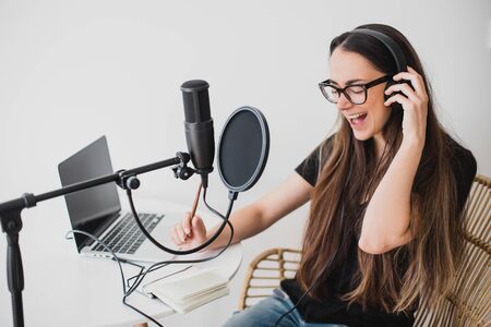 Attractive young woman blogger with long black hair recording online podcast using her laptop, headphones and professional microphone.の写真素材