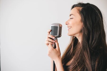 Young beautiful woman sing in vintage microphone on white background.の写真素材