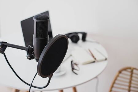 Items for recording podcast: professional microphone, earphones and laptop on white table in cozy...