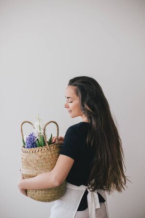 Young beautiful woman with long hair holding basket with hyacinth flowers on white background. Place for text.の写真素材