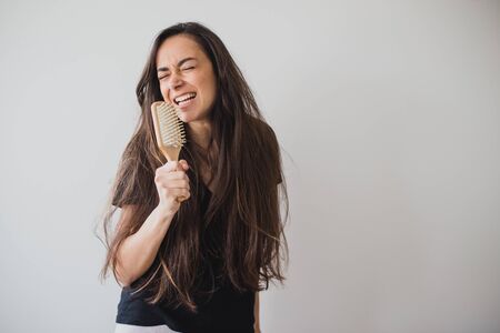 Young beautiful happy woman brushes her long healthy hair with wooden hairbrush on white background....