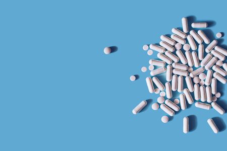 White medical pills and capsules or vitamines on blue background. Place for text.の写真素材