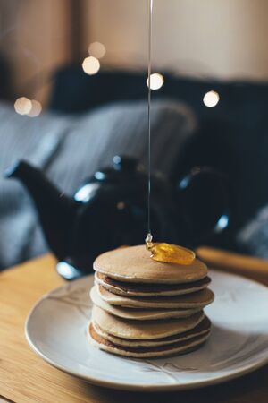 Fresh homemade banana pancakes with honey or syrop and pot with hot tea on wooden tray in cozy room.の写真素材