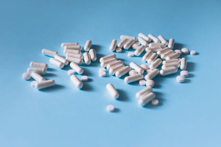 White medical pills and capsules or vitamines on blue background. Place for text.