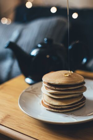 Fresh homemade banana pancakes with honey or syrop and pot with hot tea on wooden tray in cozy room.の写真素材