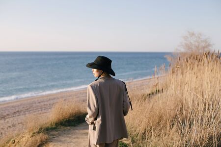 Young beautiful stylish woman wearing fashion clothes and hat posing at beach on sunset time.の写真素材