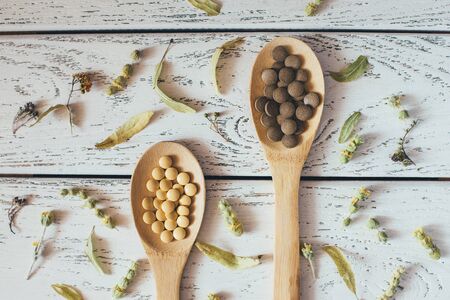 Herbal homeopathy natural pills or vitamins in wooden spoons and dry herbs on white vintage background.の写真素材