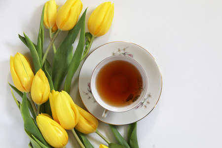 A cup of tea and bunch of yellow tulips on white background. Concept of holiday, birthday, Easter, March 8.の写真素材