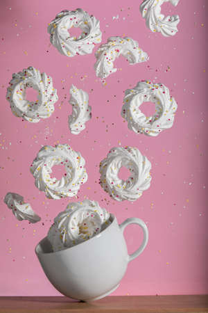 White meringues in flying motion from a white cup balancing on a table. Food levitation image on pink background.の写真素材