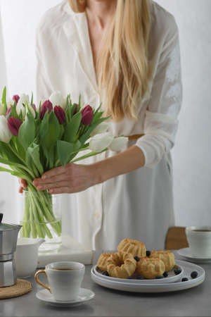Mini bundt cakes with fruits on plate, cup of coffee and girl put bouquet of tulip flowers in a vase.の写真素材