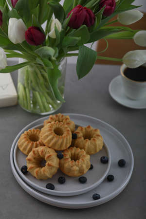 Mini bundt cakes with fruits on plate, cup of coffe and bouquet of tulips. Breakfastの写真素材