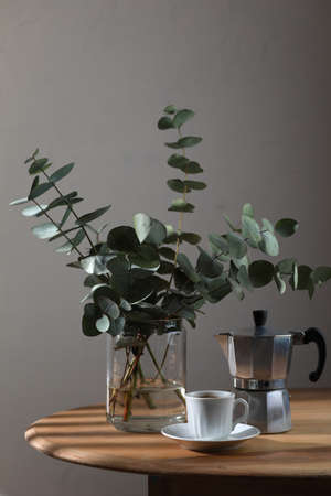 Cup of coffee, geyser coffee maker and bunch of eucalyptus on wooden table. Copy spaceの写真素材
