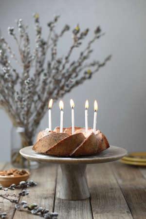 Homemade nuts bundt cake with powder sugar, candles and bouquet of fresh willows on wooden table. Rustic styleの写真素材