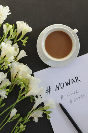 No War message on white paper, cup of coffee and white flowers on dark background. Copy space