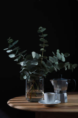Cup of coffee, geyser coffee maker and bunch of eucalyptus on wooden table. Copy spaceの写真素材