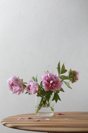 Pastel pink peony flowers bouquet in a glass vase on wooden table.の写真素材